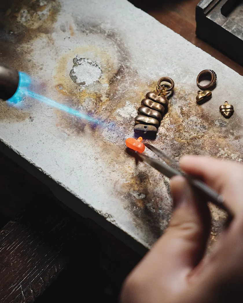 Soplete con llama azul dirigida a piezas de metal sobre un ladrillo refractario, mientras una mano acerca una varilla con fundente